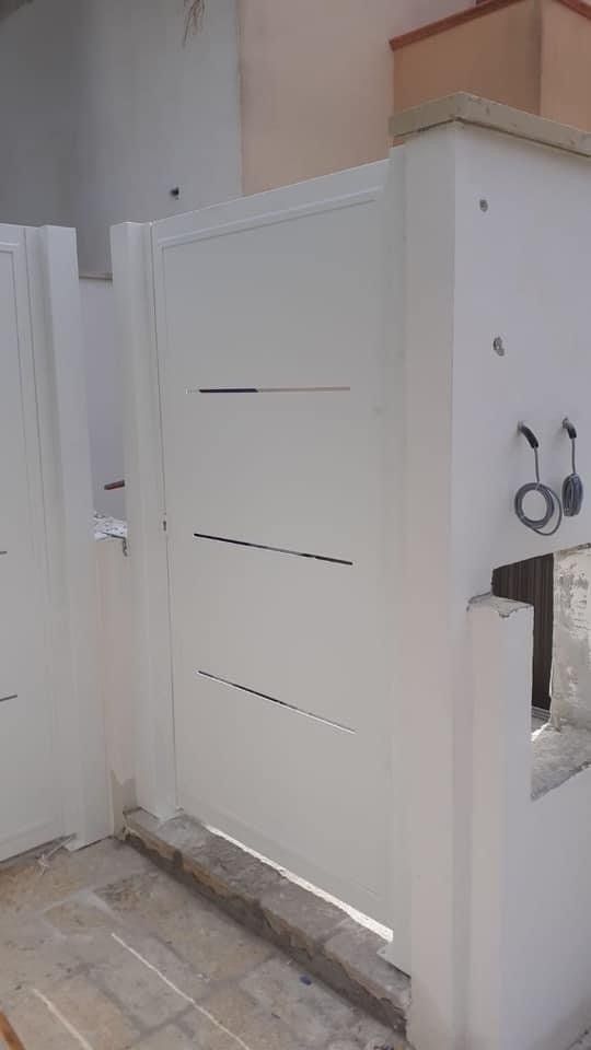 Cancello in metallo bianco con tre fessure orizzontali, accanto a un pilastro di cemento, all'esterno.