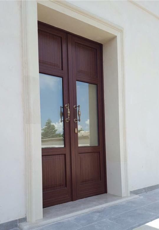 Doppie porte marroni con pannelli in vetro, maniglie in ottone, inserite in una cornice bianca, su una soglia grigio chiaro.