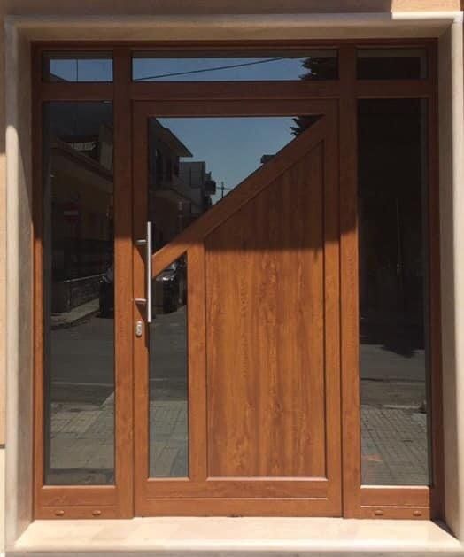 Porta in legno con pannelli in vetro, incastonata in una cornice beige. La luce del sole crea ombre.