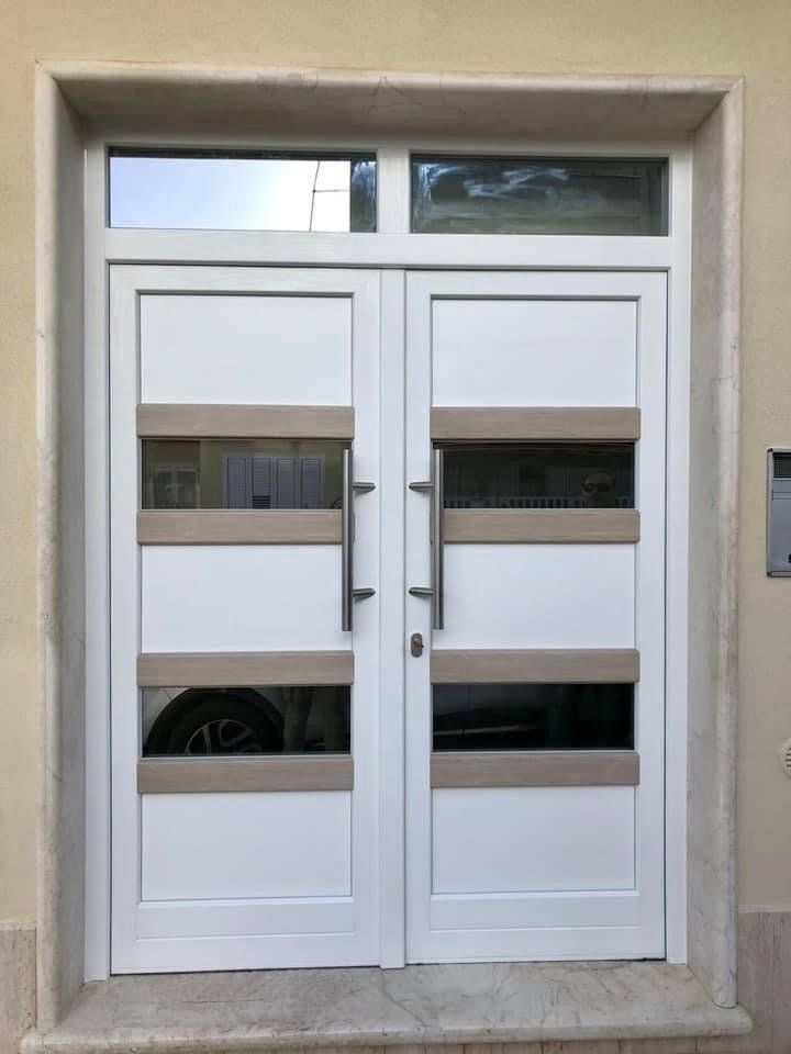 Porte doppie bianche con pannelli in vetro e dettagli in legno chiaro, sotto una finestra, in un ingresso beige.