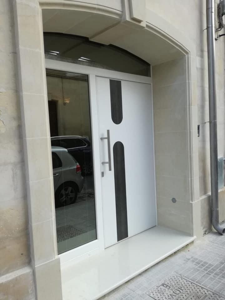 Porta bianca con dettagli neri, maniglie argentate e pannello di vetro adiacente in un portale in pietra chiara.