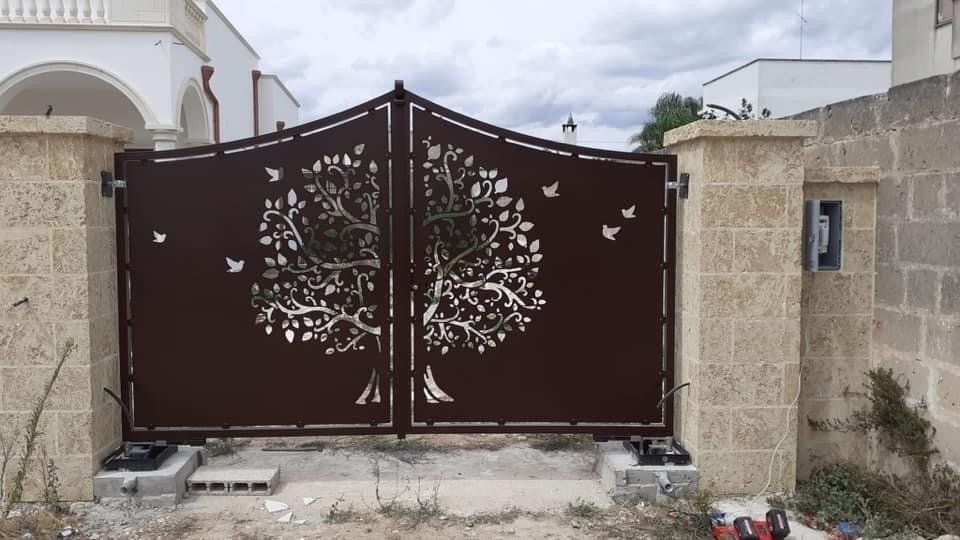 Cancello in metallo marrone con sagome di alberi e uccelli, tra pilastri in pietra.
