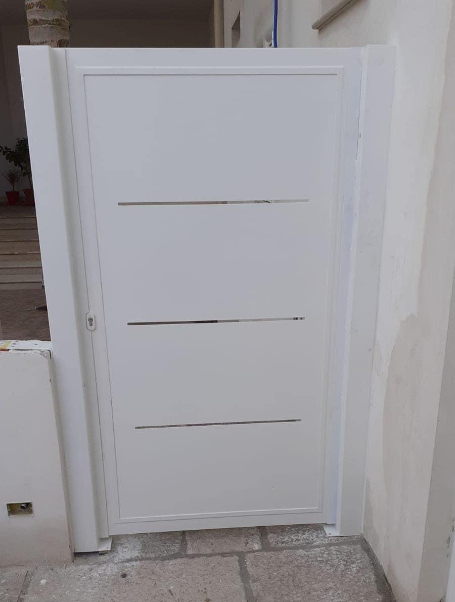 Cancello in metallo bianco con fessure orizzontali, inserito in un muro bianco, su un patio in pietra.