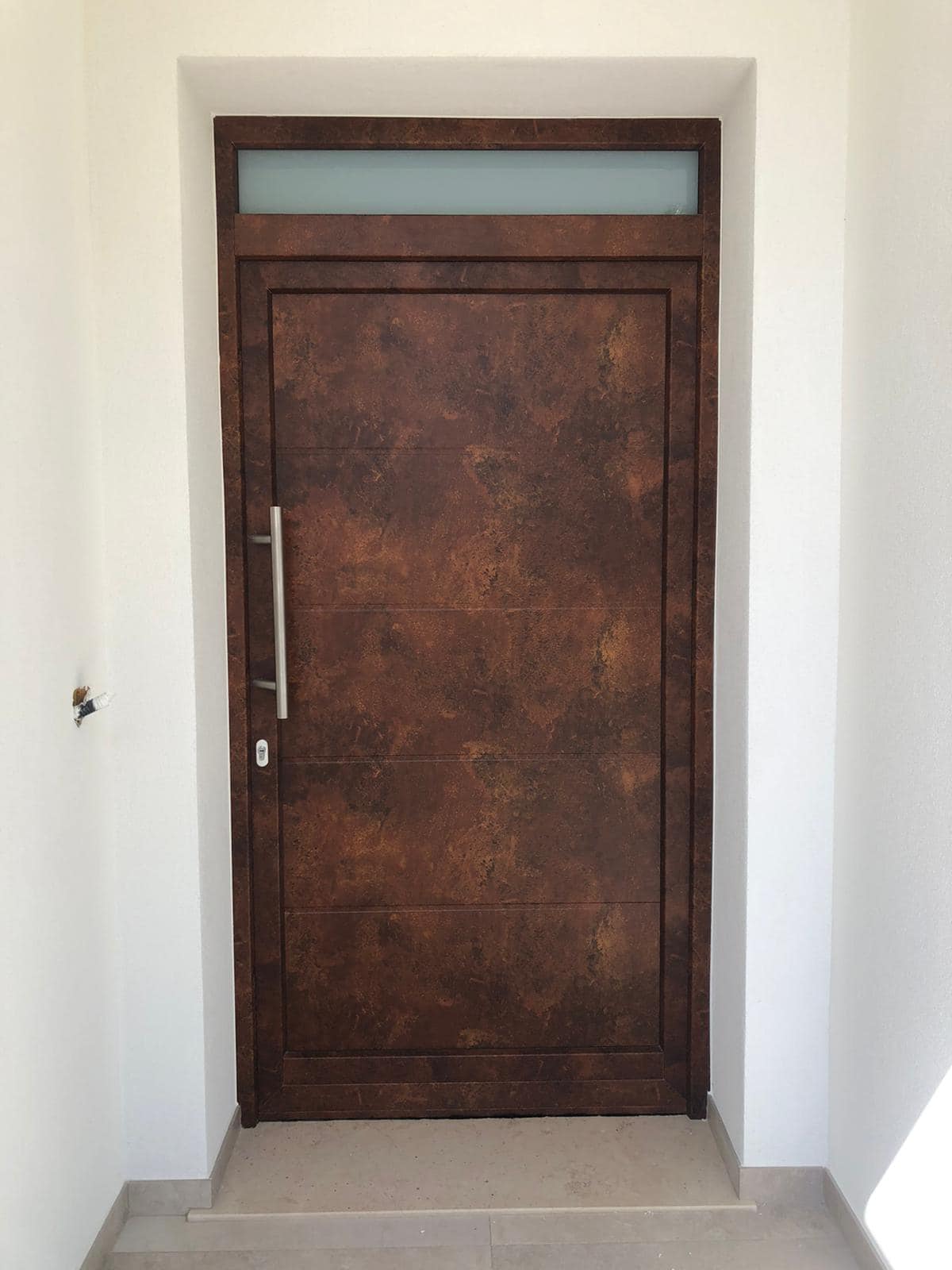 Una porta in metallo marrone con un sopraluce in vetro smerigliato, incassata in un vano porta bianco