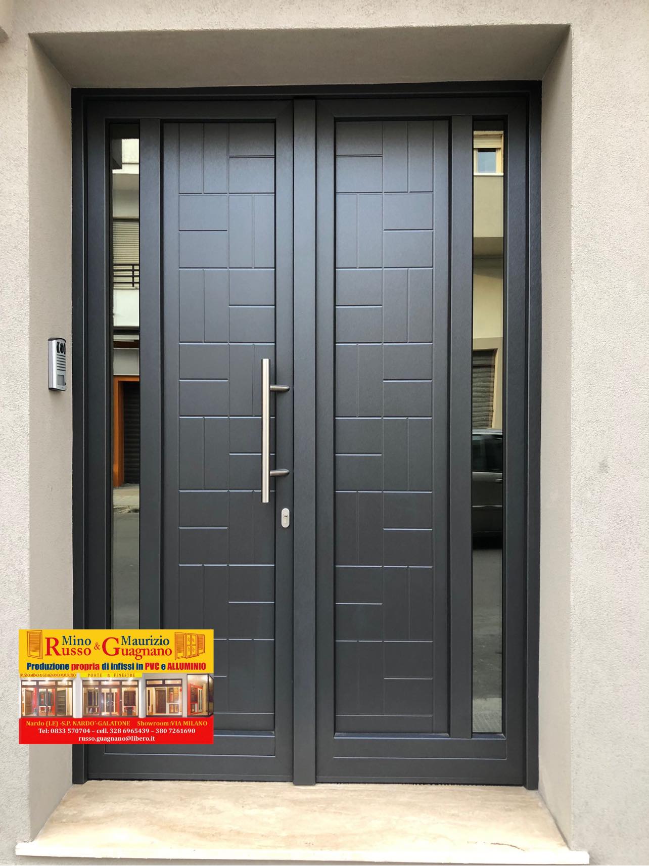 Porta doppia grigia con pannelli laterali in vetro e maniglia lunga, montata su una parete in stucco chiaro.