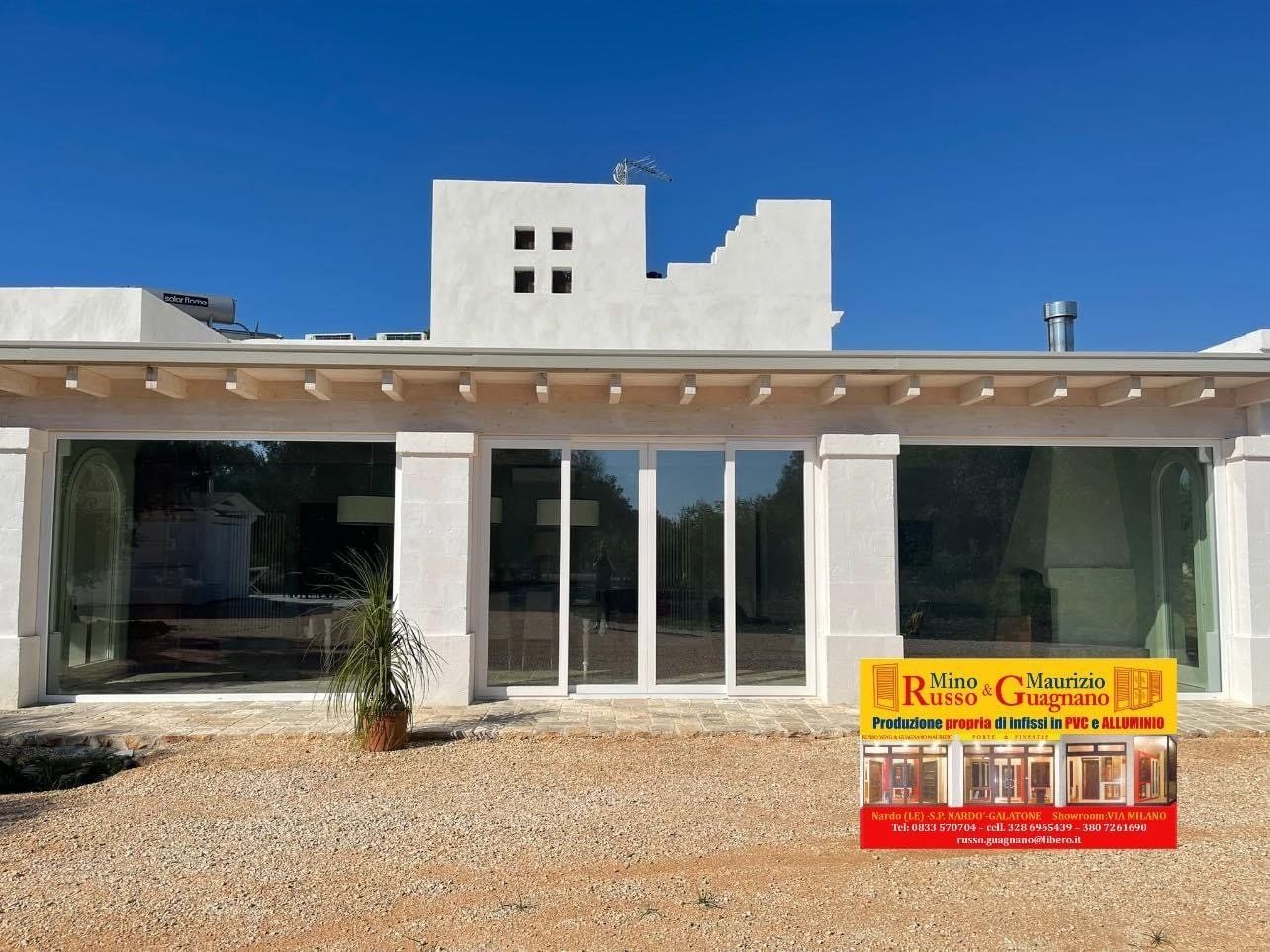 Edificio bianco con grandi finestre, un'insegna e una pianta all'esterno. Giornata di sole.