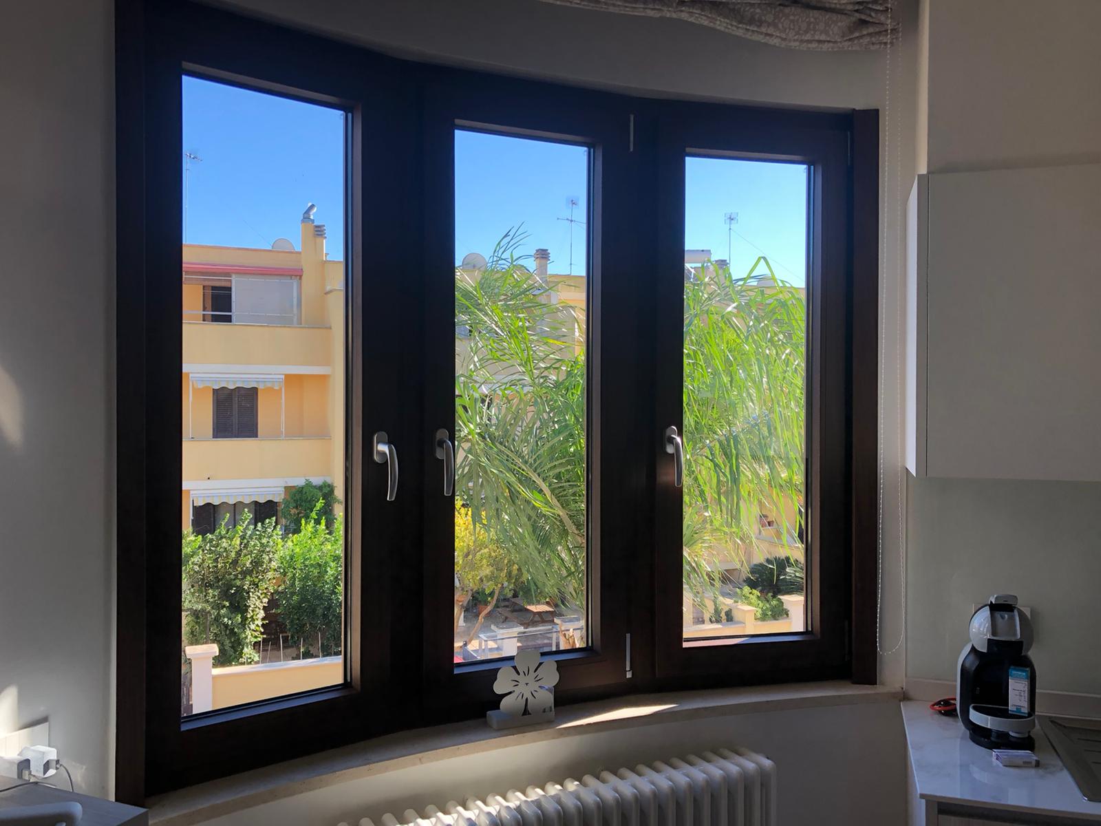 Una finestra curva con cornice scura che offre una vista su edifici, alberi e un cielo azzurro brillante.