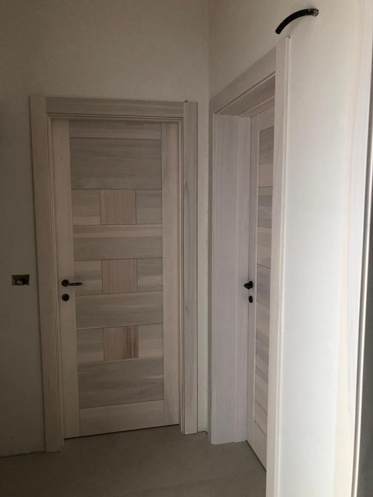 Due porte di legno chiaro con maniglie scure in un corridoio dalle pareti bianche.