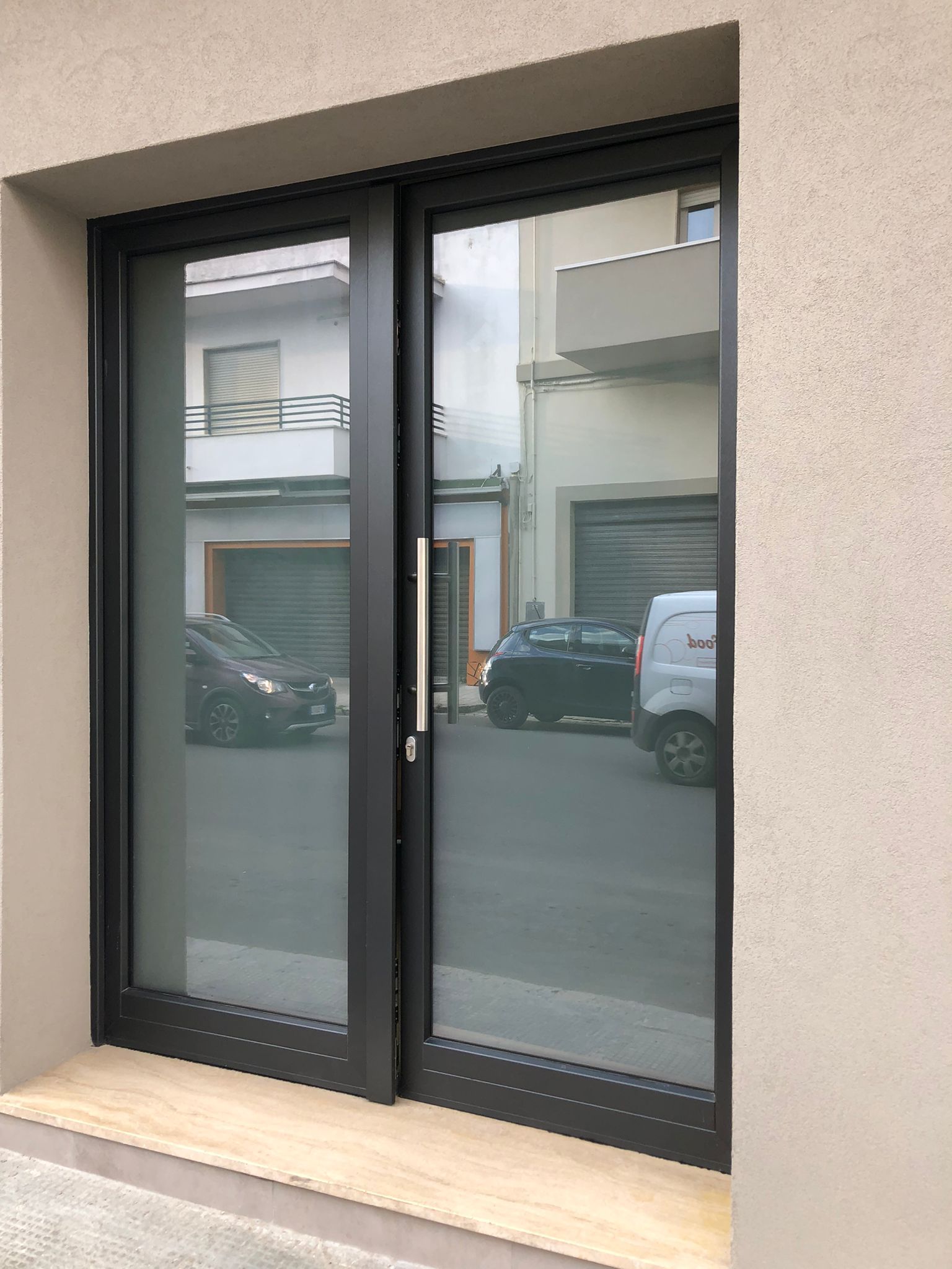 Porte a due ante in vetro con cornice nera e maniglia argentata, incastonate in una parete beige. 