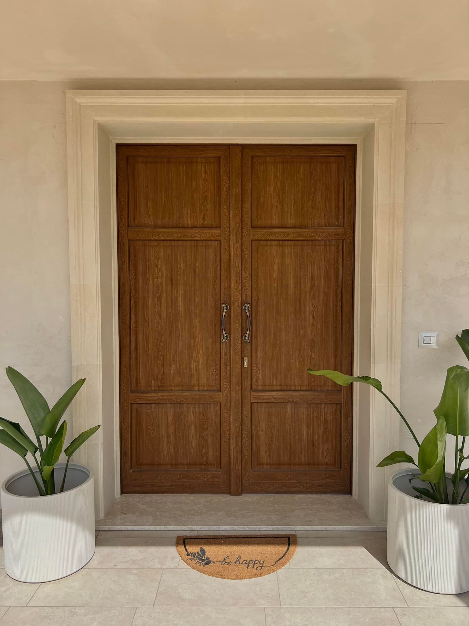 Doppie porte in legno con fioriere in pietra e zerbino.
