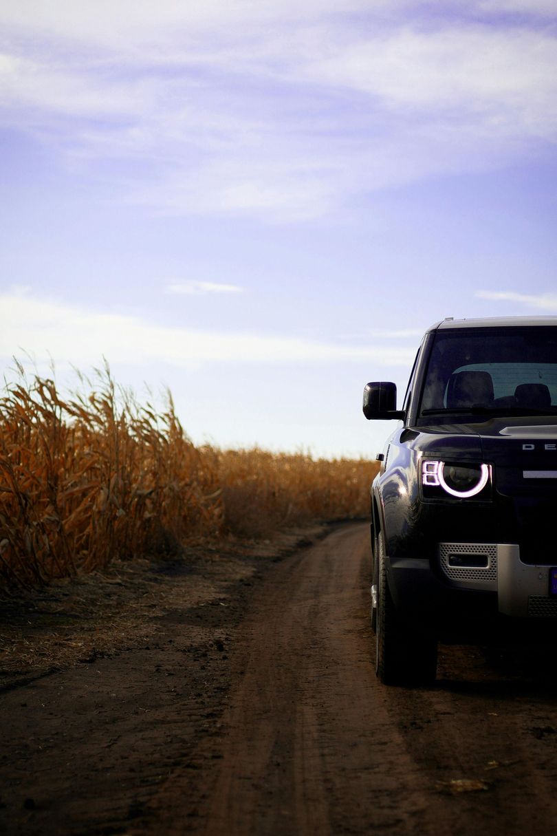 Black Land Rover Defender on a dirt road, alongside tall brown grass, under a blue sky.