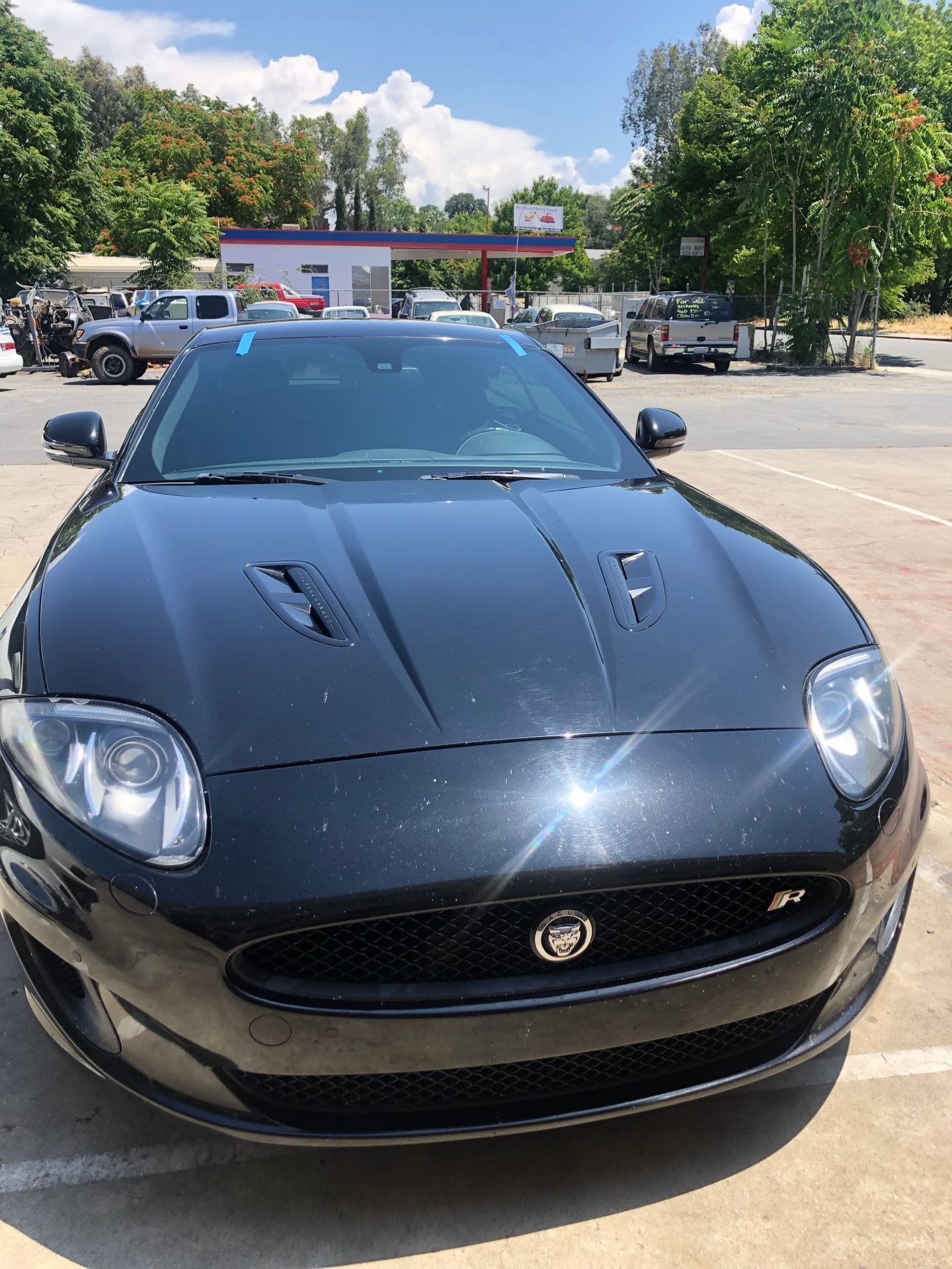 Black Jaguar XKR parked at a gas station on a sunny day.