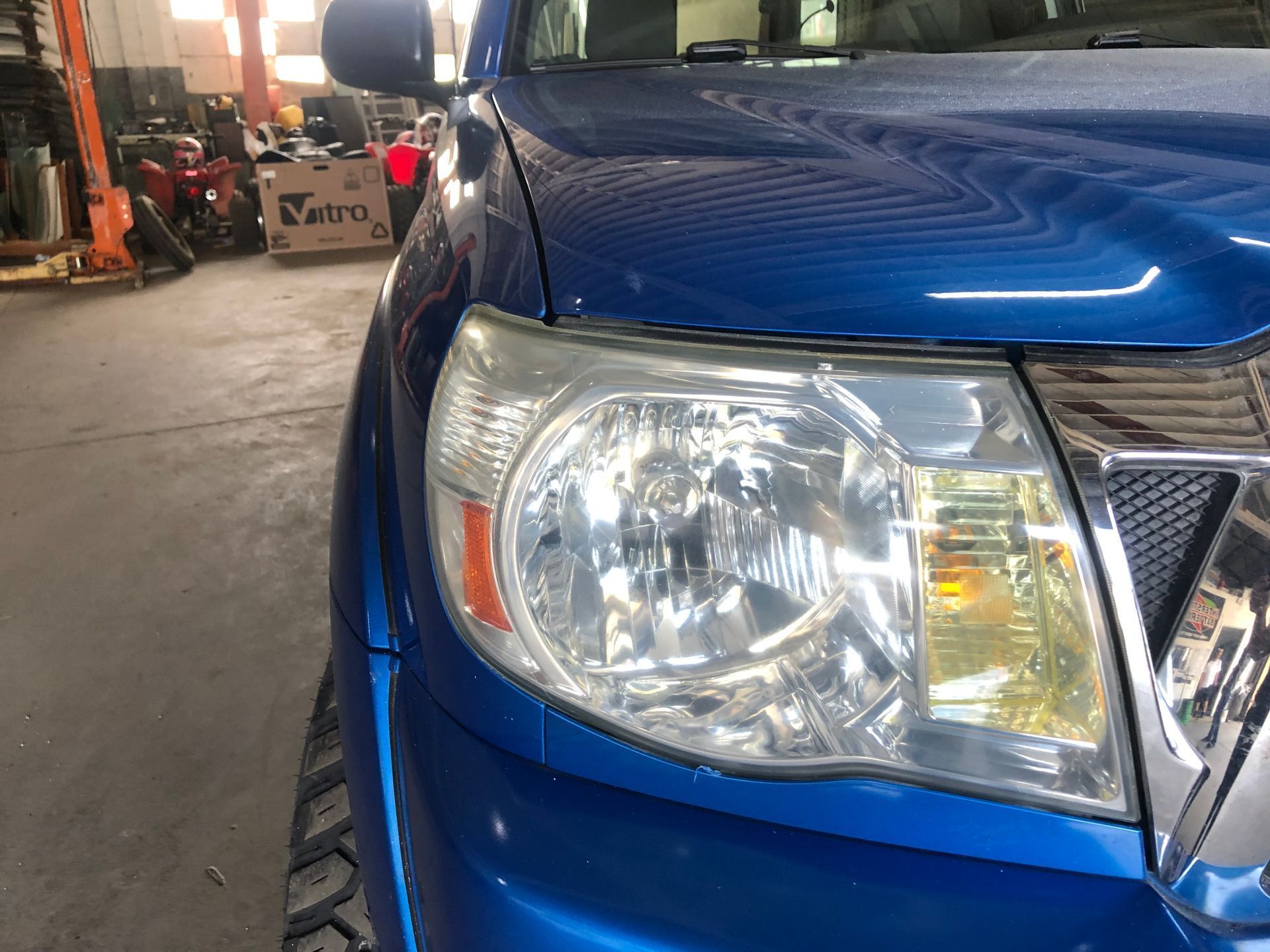 Blue pickup truck headlight, close-up.  Headlight is yellowed and slightly hazy.  Silver grill visible.