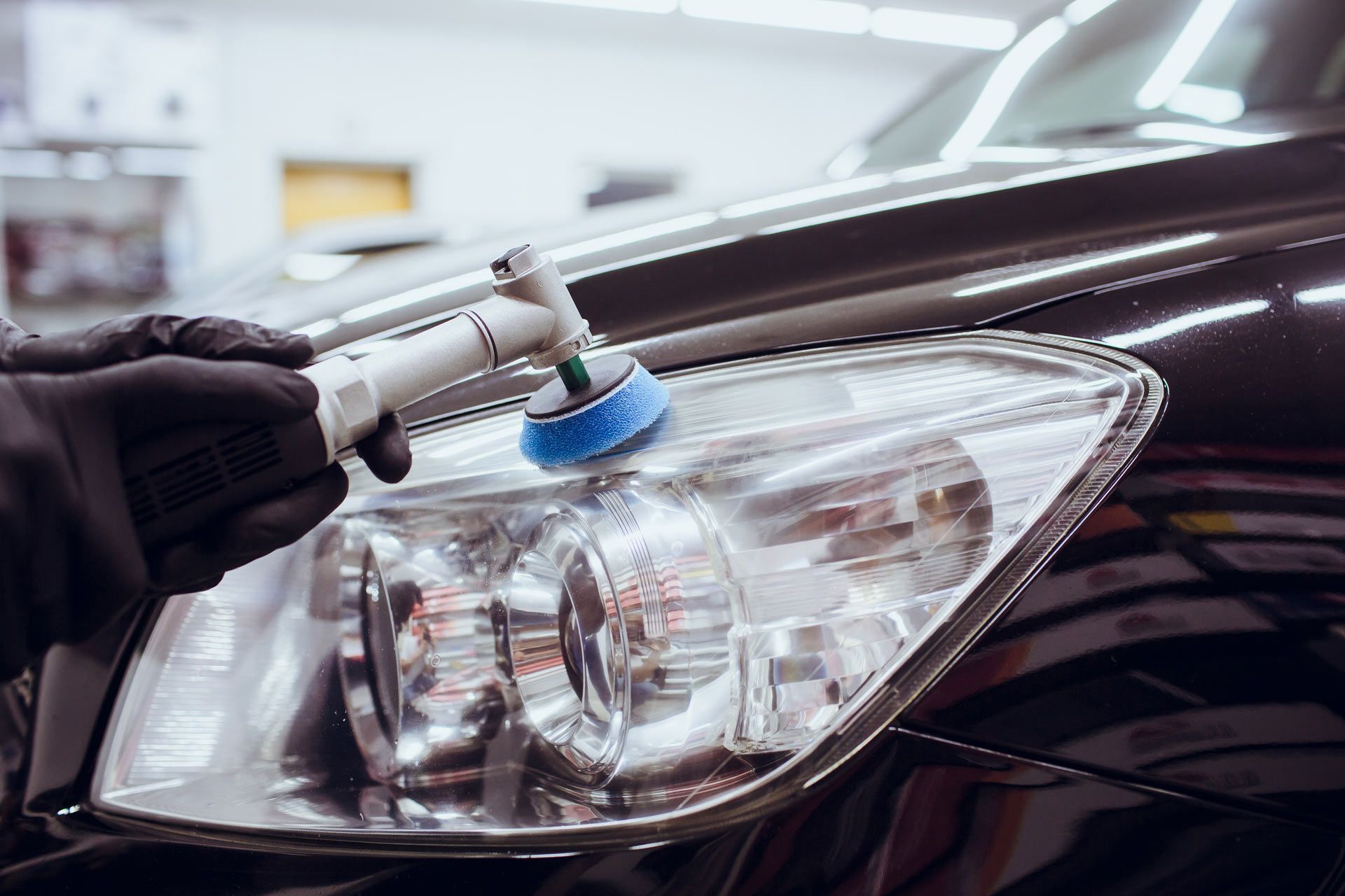 Black-gloved hand using a buffing tool to polish a car's headlight.