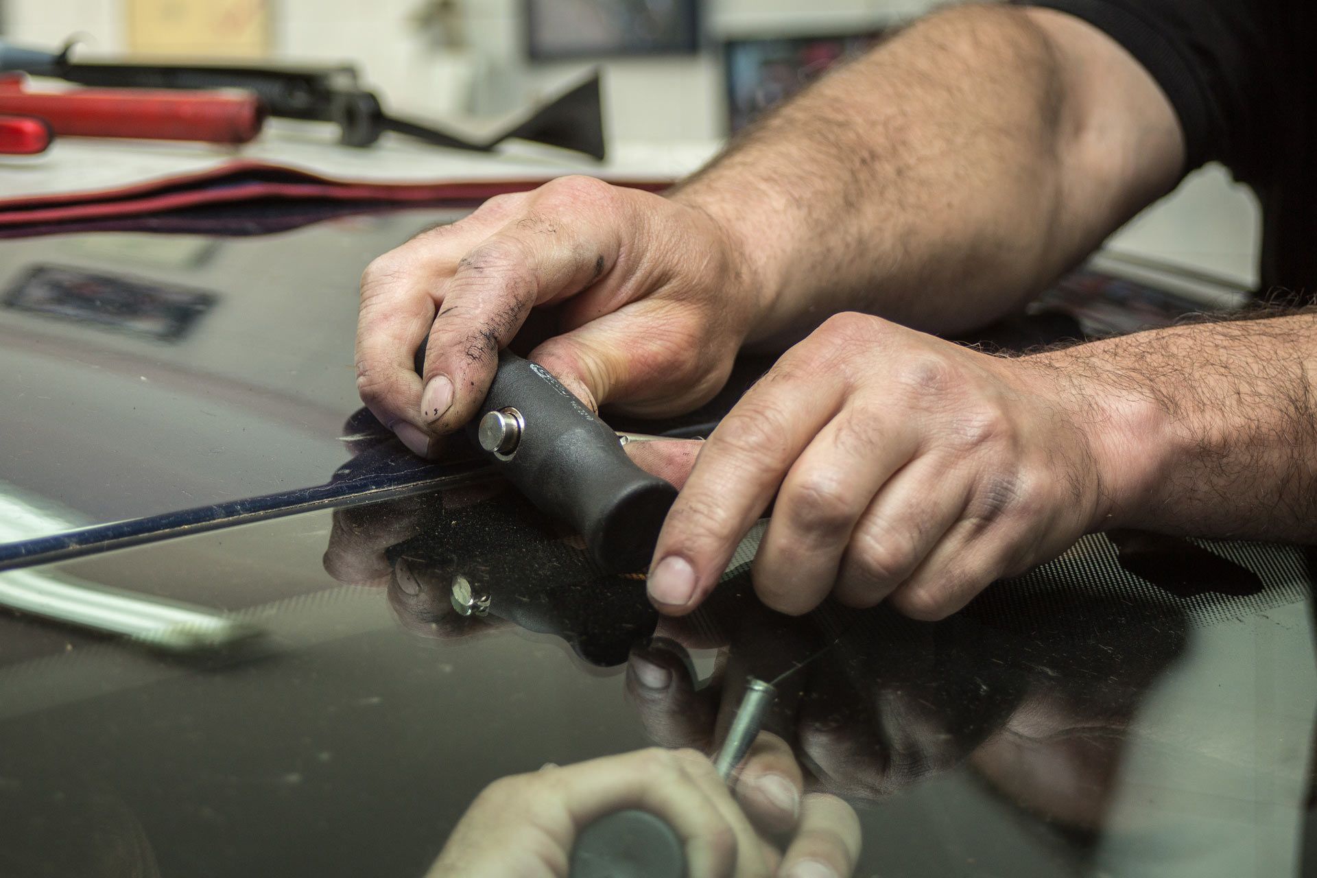 Hands repairing a windshield with tools.