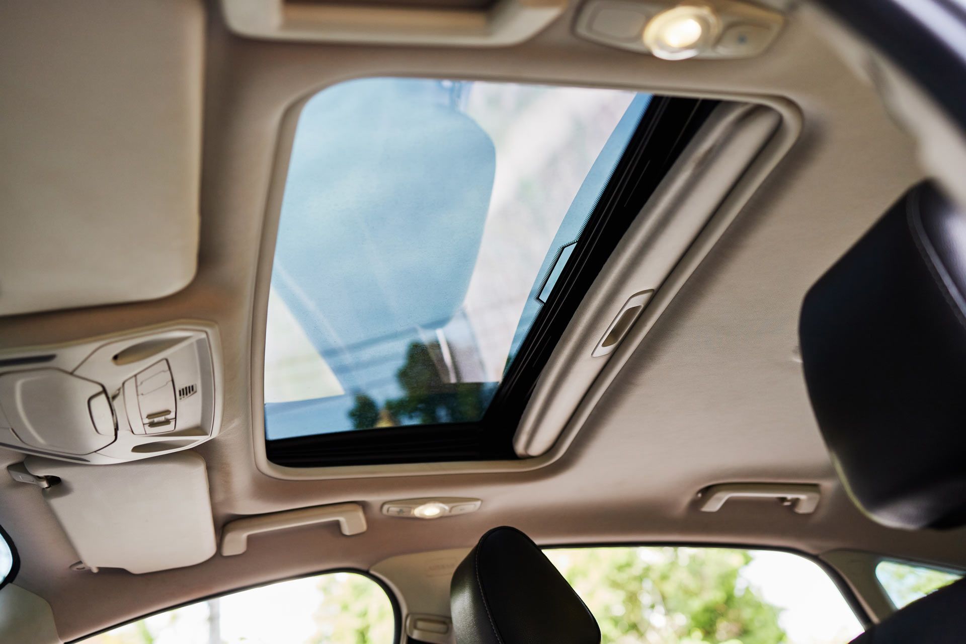 Interior car shot of open sunroof, revealing blue sky and trees.