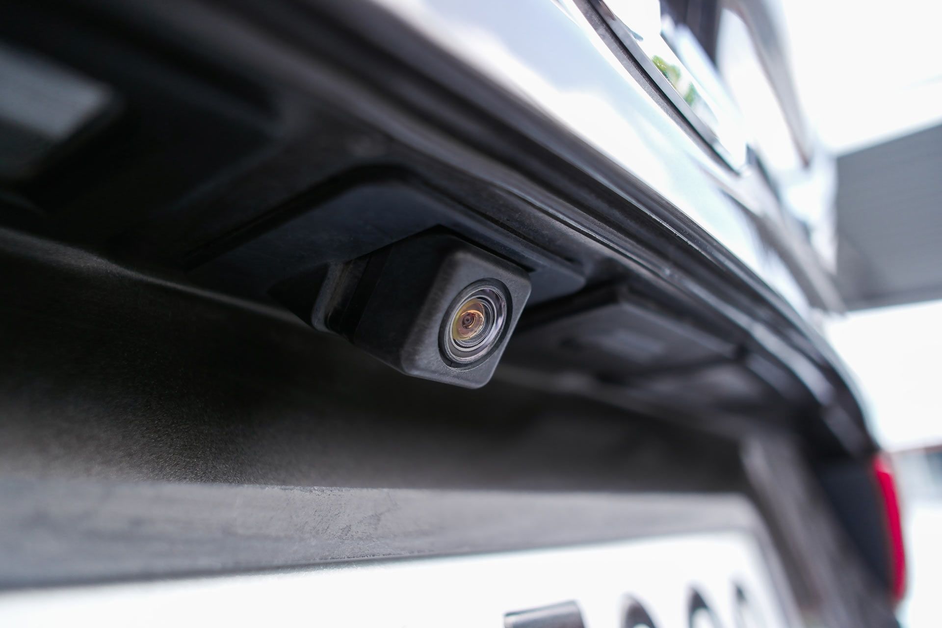 Close-up of a car's rear bumper with a backup camera. Black, rectangular camera lens is centered on the bumper.