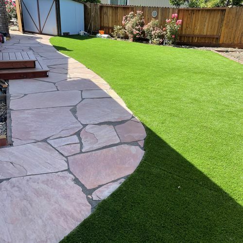 A backyard with a stone walkway and a lush green lawn.