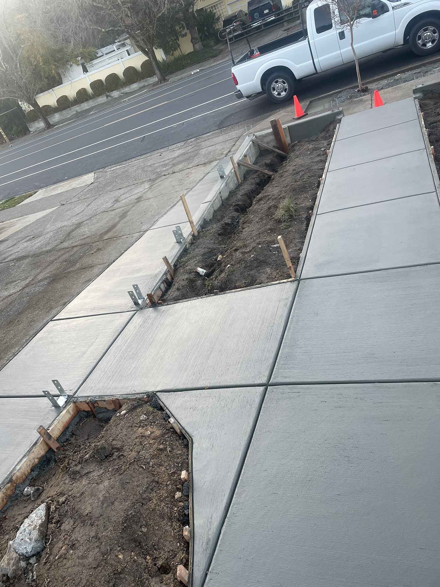 A white truck is parked on the side of the road next to a concrete sidewalk.