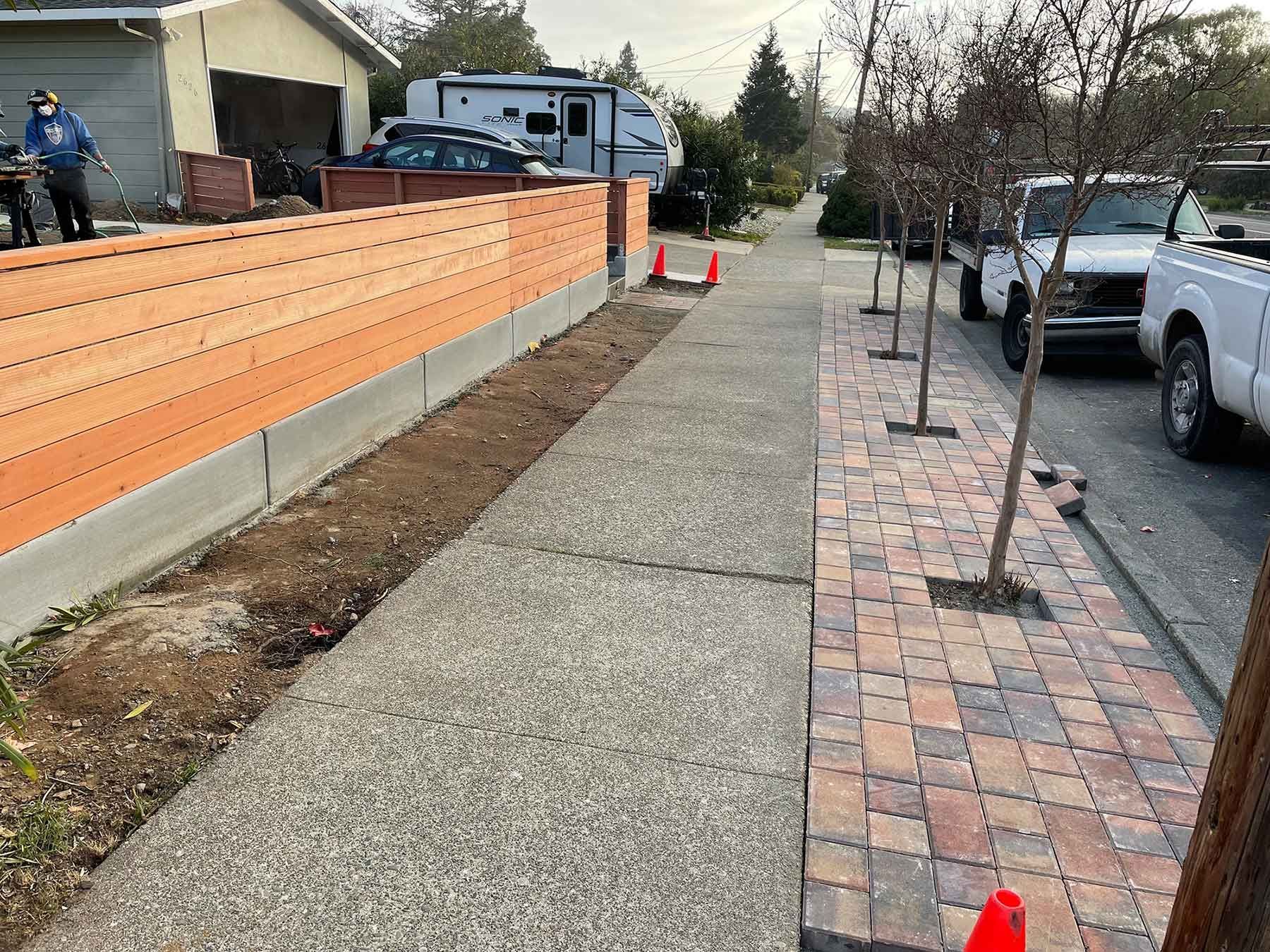 A wooden fence is being built next to a brick sidewalk.