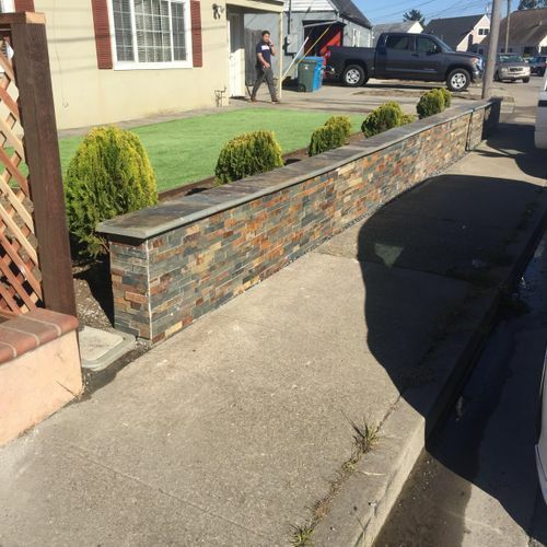 A brick wall is along the sidewalk in front of a house.