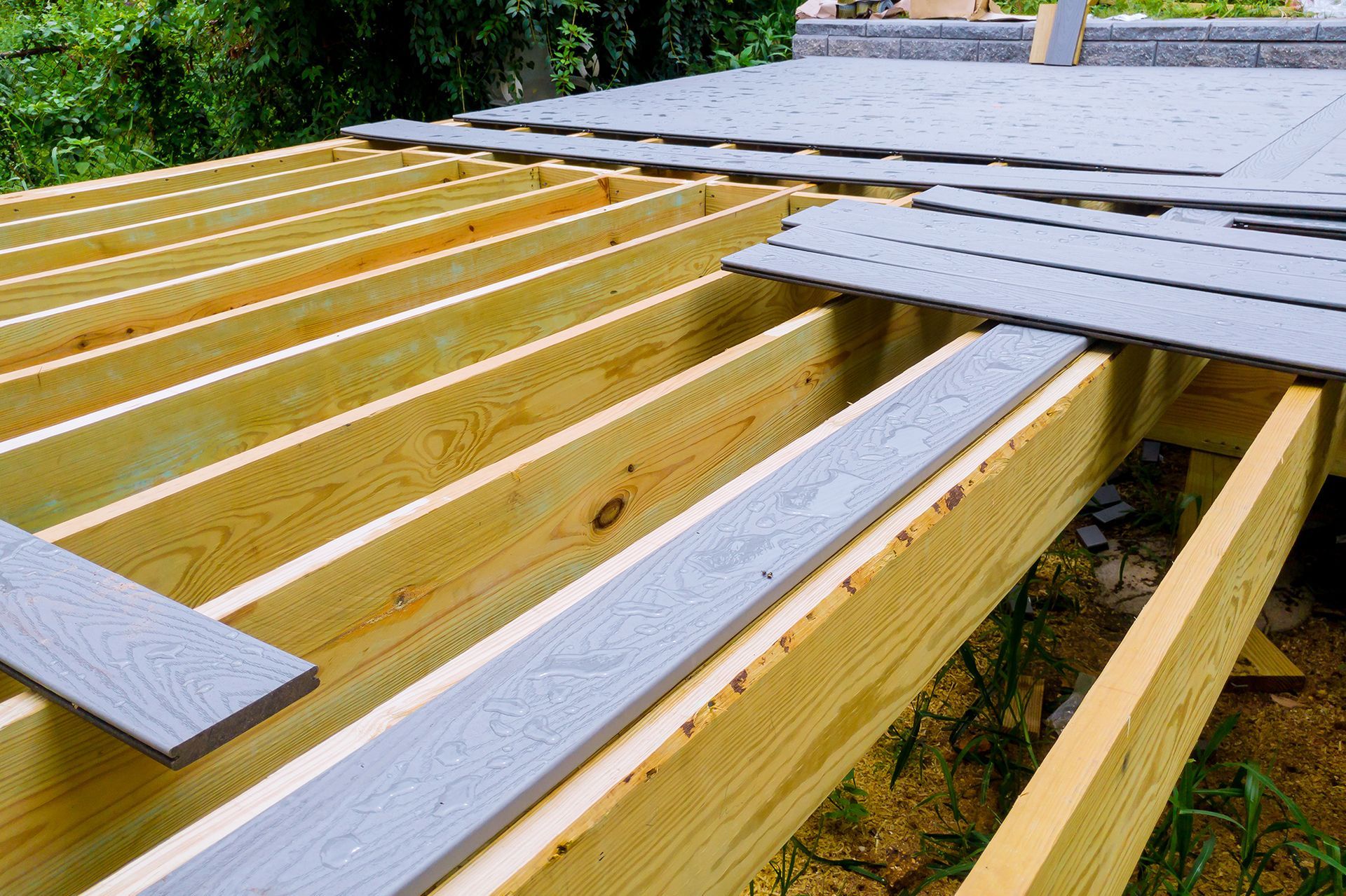 Wooden deck construction: Light gray composite decking being installed on yellow lumber frame.