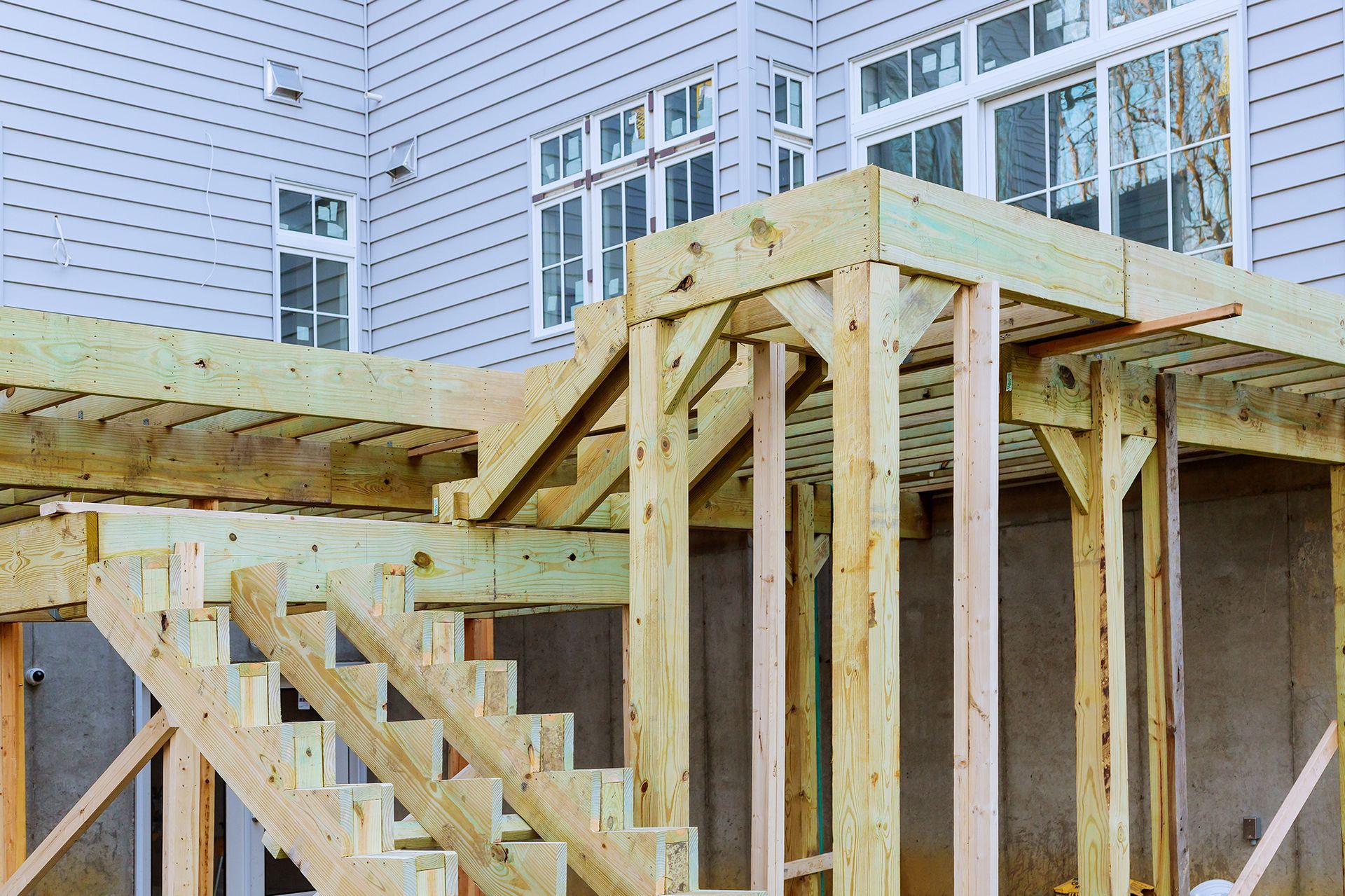 Wooden deck construction with stairs and supports against a light-colored house.