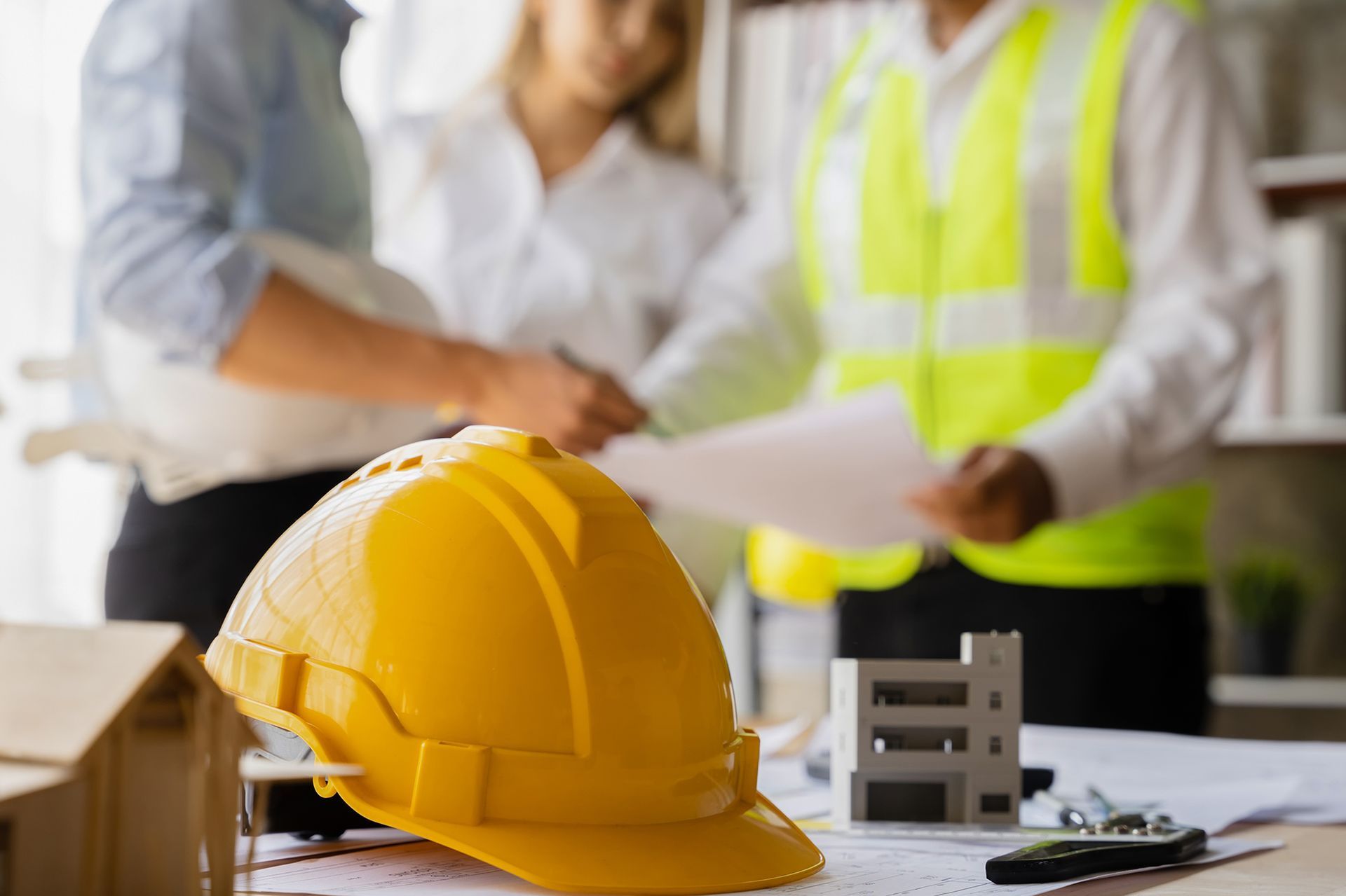 Yellow hard hat on a table with construction workers reviewing blueprints.