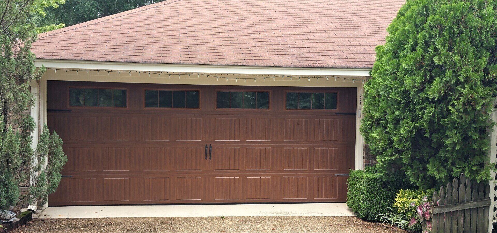 A brown garage door is sitting in front of a house with a red roof.