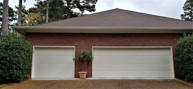 A brick garage with two white doors, a potted plant between them, and trees in the background.