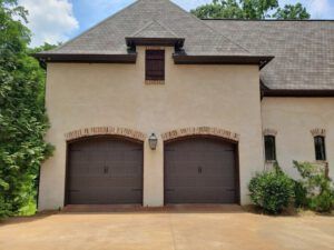 A large white house with two brown garage doors and a roof.