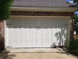 A white garage door is sitting in front of a brick house.