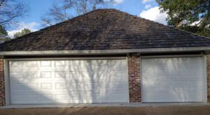 A garage with three white garage doors and a brick roof.
