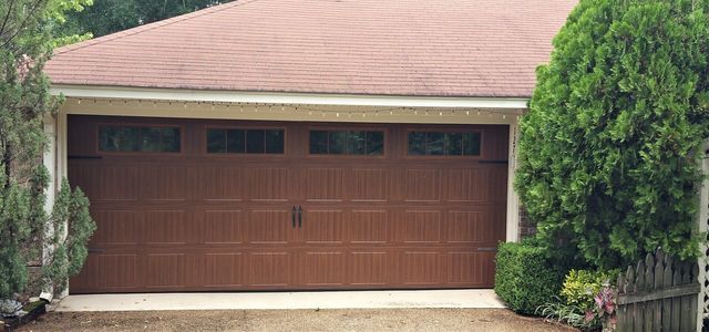 A brown garage door is in front of a house with a red roof.