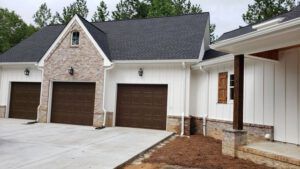 A large white house with three garage doors and a black roof.
