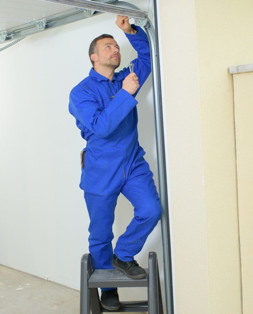 A man is standing on a ladder fixing a garage door.