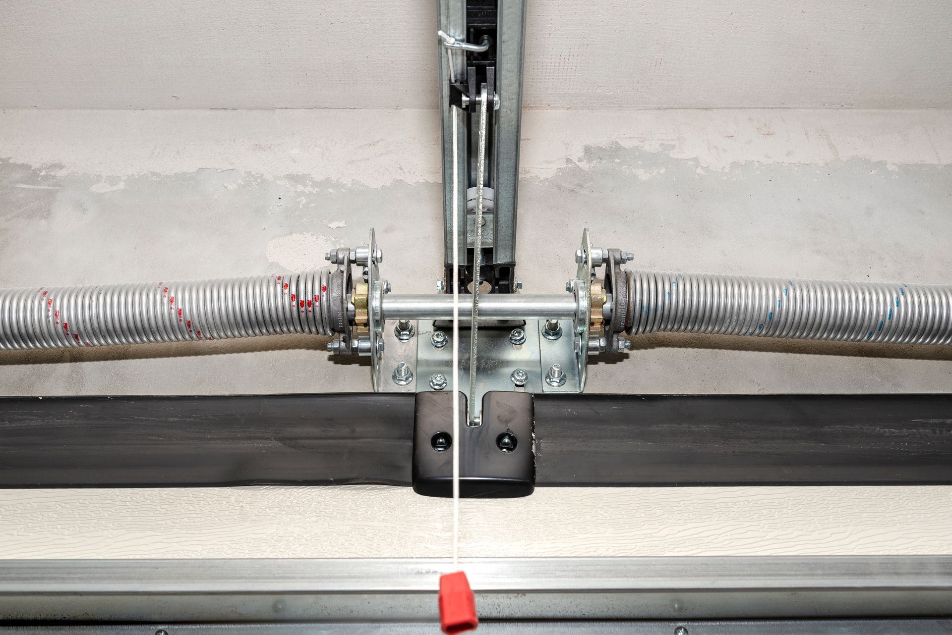 A close up of a garage door spring with a red cord attached to it.
