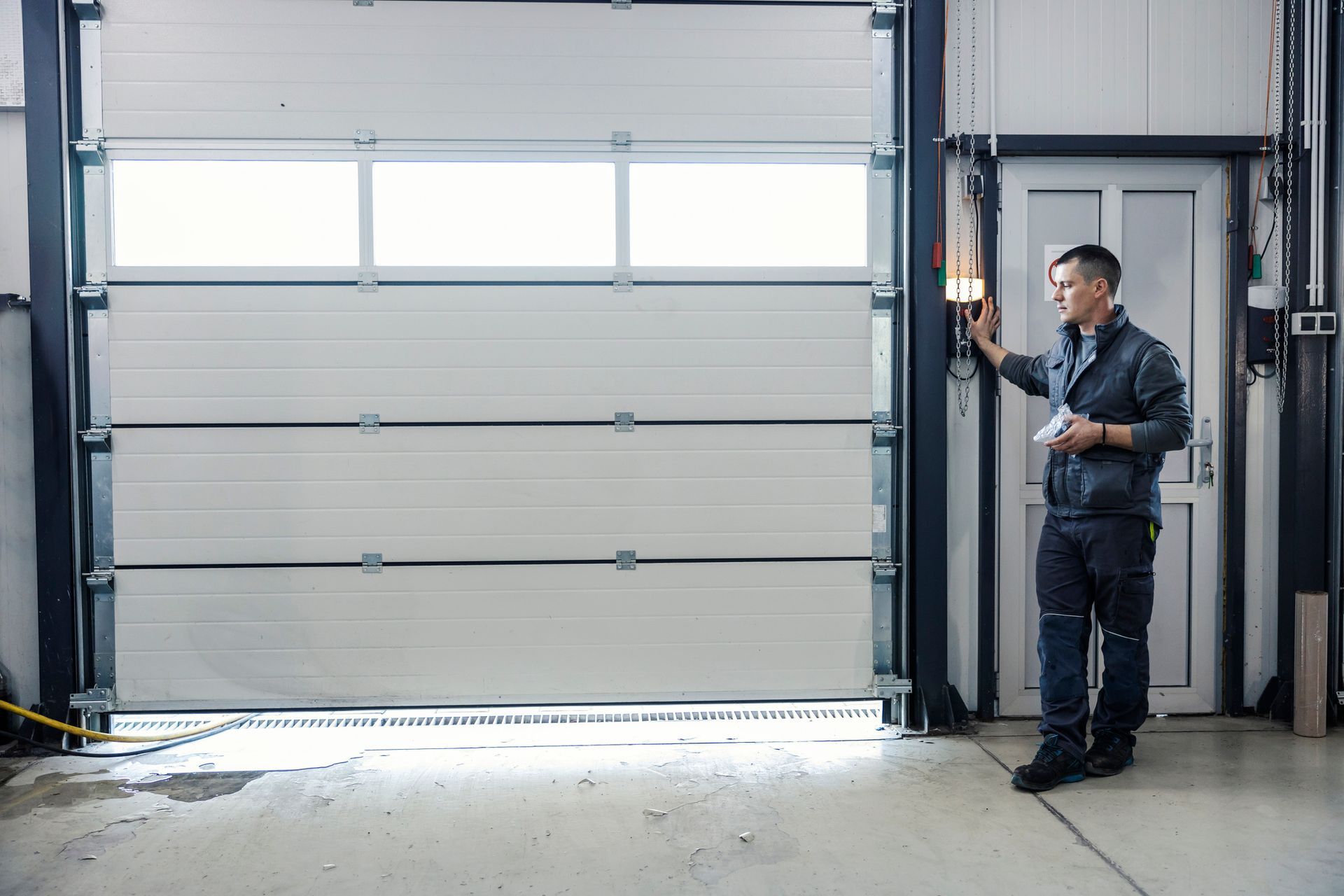 Person operating a wall control near a large garage door inside an industrial space.
