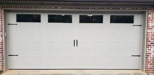 A white garage door with black windows on the upper part, on a brick wall.