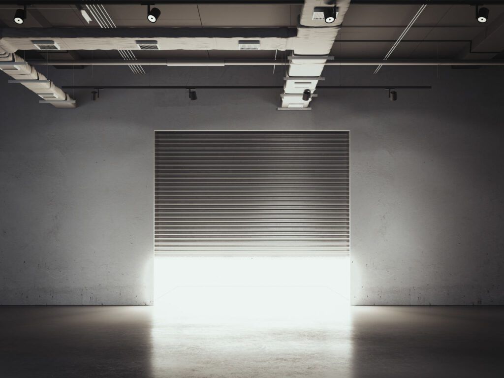 A warehouse with a garage door open and a light coming through it.