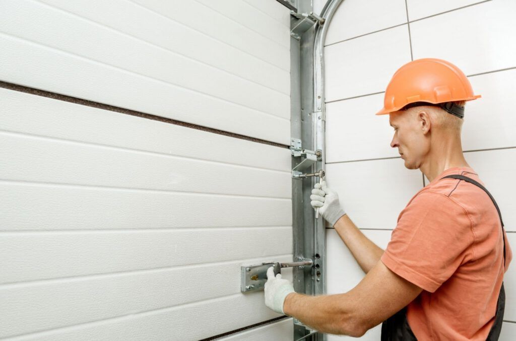 A man wearing a hard hat is working on a garage door.