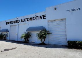 Preferred Automotive building exterior with garage doors, palm trees, and blue sky.