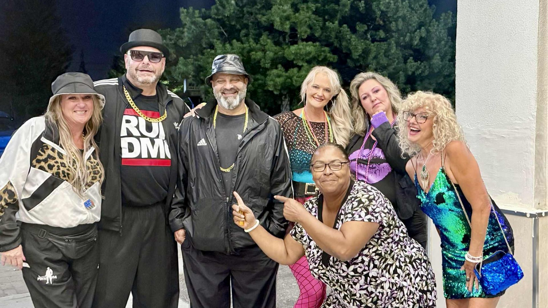 Group of people in 80s themed costumes, posing outdoors at night.