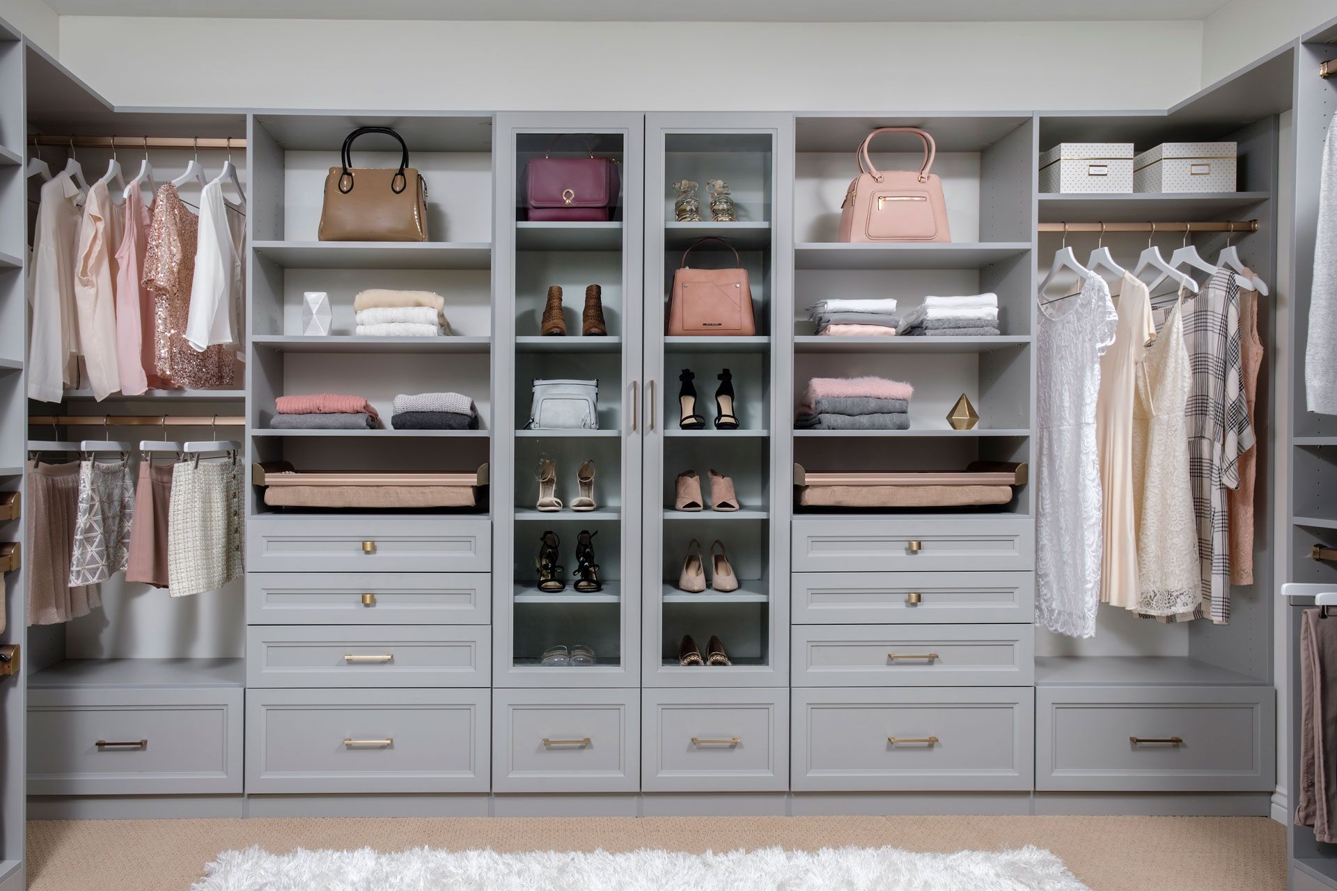 Gray walk-in closet with shelves, drawers, and hanging rods filled with clothing, purses, and shoes.
