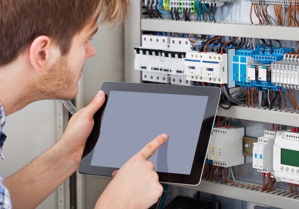 A Man Is Looking At A Tablet In Front Of An Electrical Cabinet — RAFFBRO Electrical Solar & Air Conditioning In Corowa, NSW