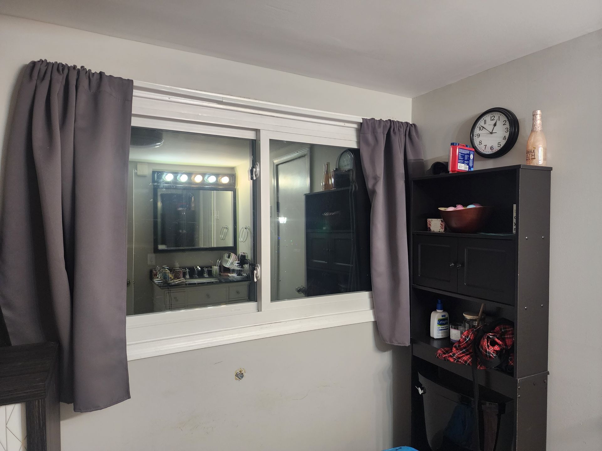 A bedroom with a large window and a clock on the wall.