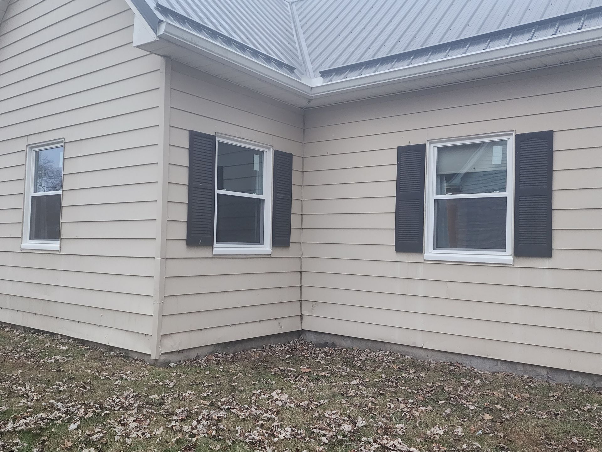 The side of a house with black shutters on the windows.