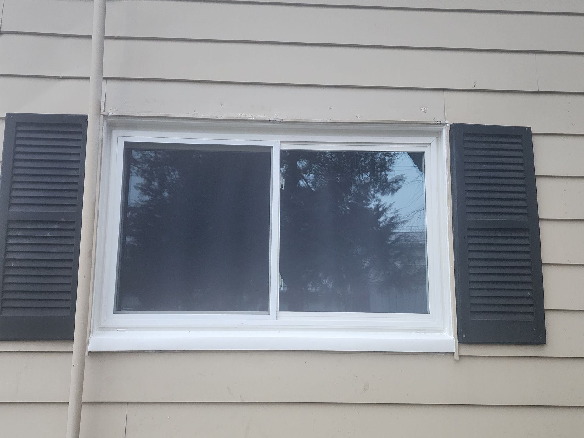 A white window with black shutters on the side of a house.