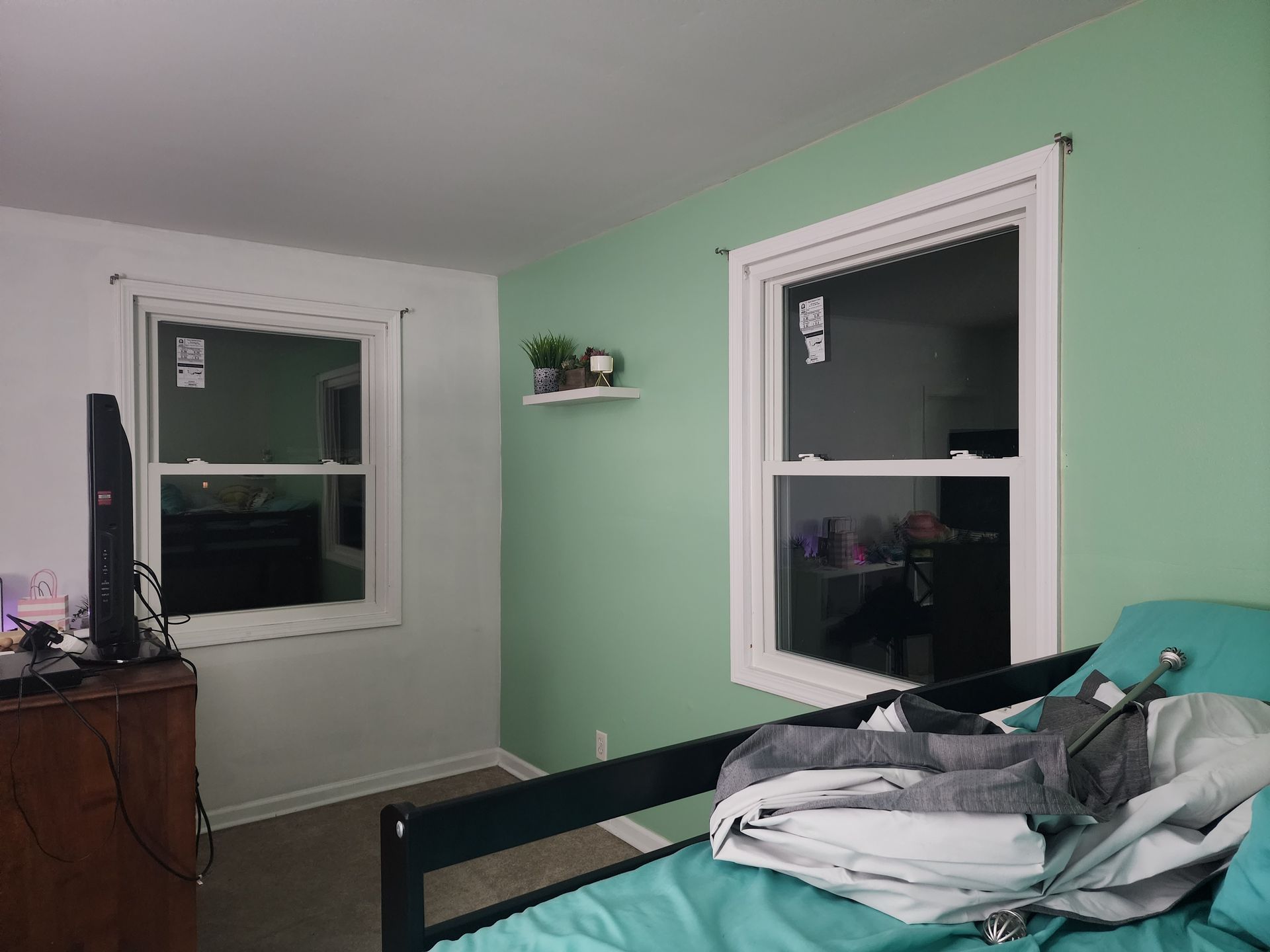 A bedroom with a bed , dresser , television and two windows.