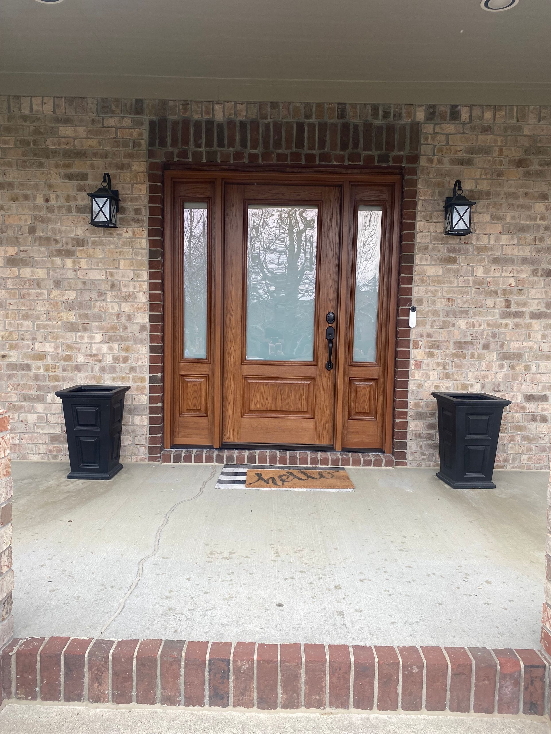The front door of a brick house with a wooden door and two planters on the porch.